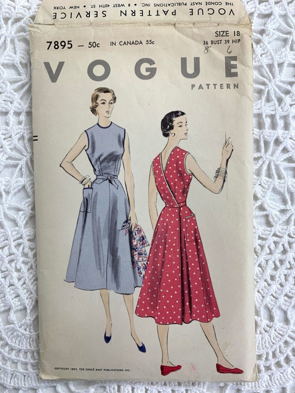 Two women in 1950s back-wrap sleeveless dresses are looking off into the distance. The woman in the blue dress has a supercilious look on her face; the woman in the red dress looks mildly amused.